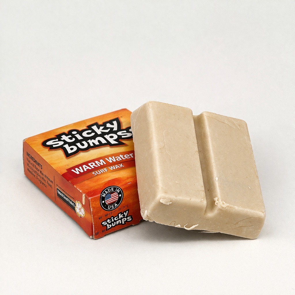 Sticky Bump Surf-Wax – warm Water Eine kleine Pappverpackung in Orange mit der Aufschrift ‚Sticky bumps Warm water‘ liegt vor einem weißen Hintergrund. Das Produkt ist obendrauf sichtbar.